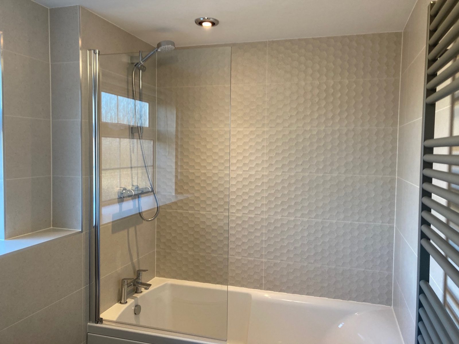 Bathroom with textured feature wall tiles and a bath with a glass shower screen