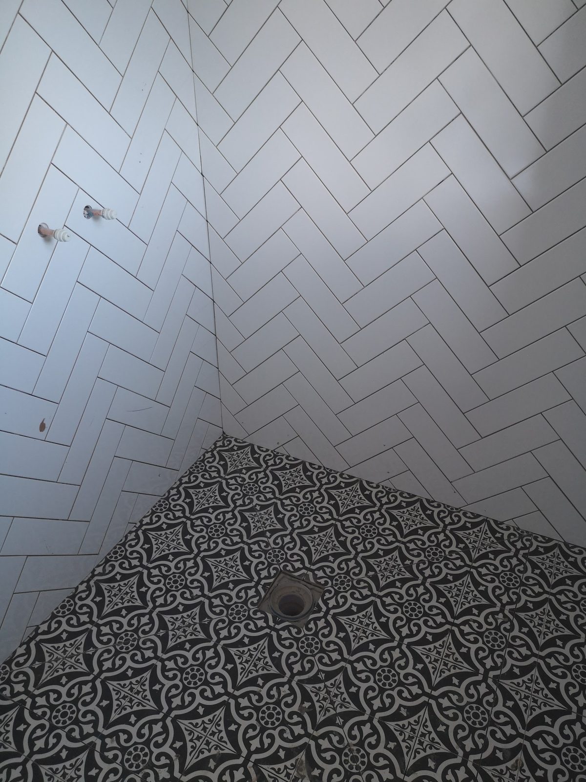 Shower with white herringbone wall tiles above a black patterned floor